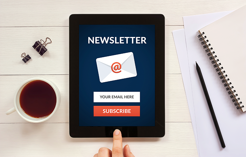 tablet on a desk, surrounded by a cup of tea and stationary, presenting a registration to a newsletter 